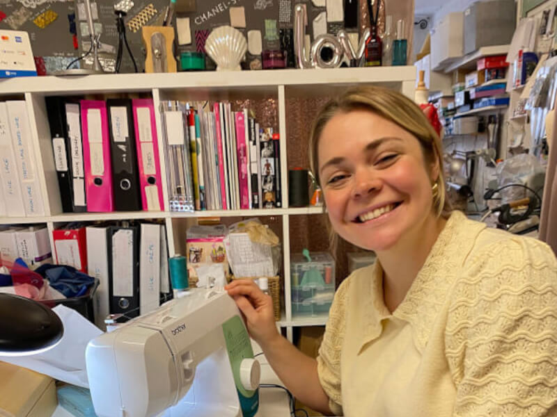 A woman in a yellow top smiles beside a white sewing machine